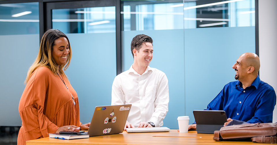Three Capital One associates laugh around a meeting table with their laptops